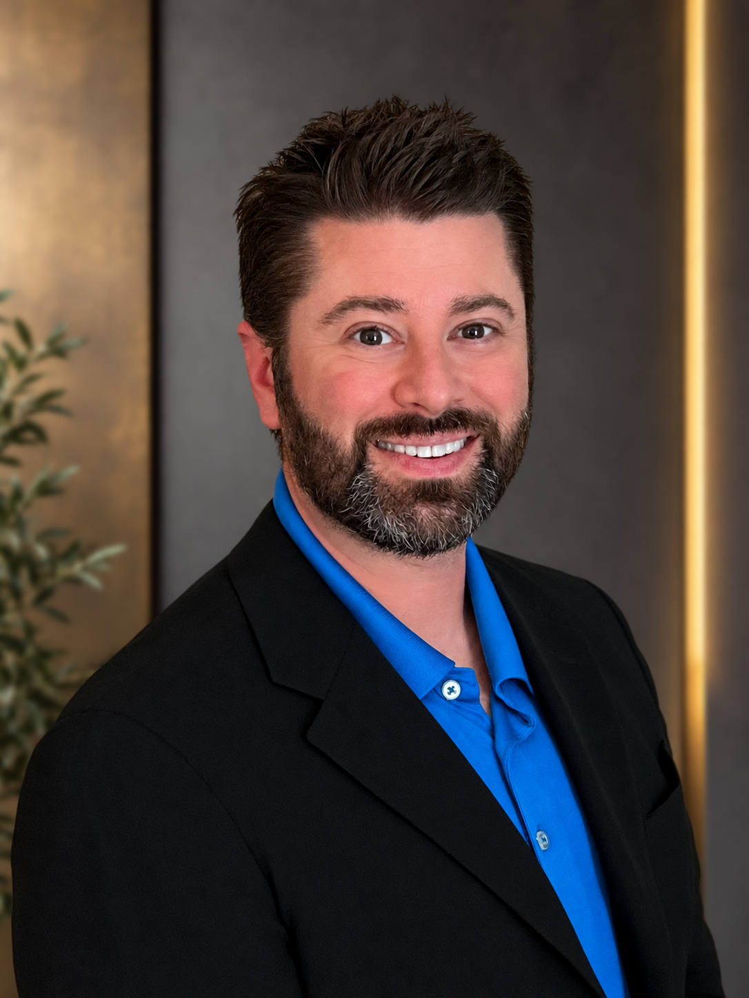 Adam Hunt, smiling in a black blazer and blue shirt